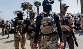 Masked ICE agents in military-style gear patrol a Southern California street during a June 2025 immigration raid (Bell, CA). Such scenes have become disturbingly common as federal raids sweep through communities.